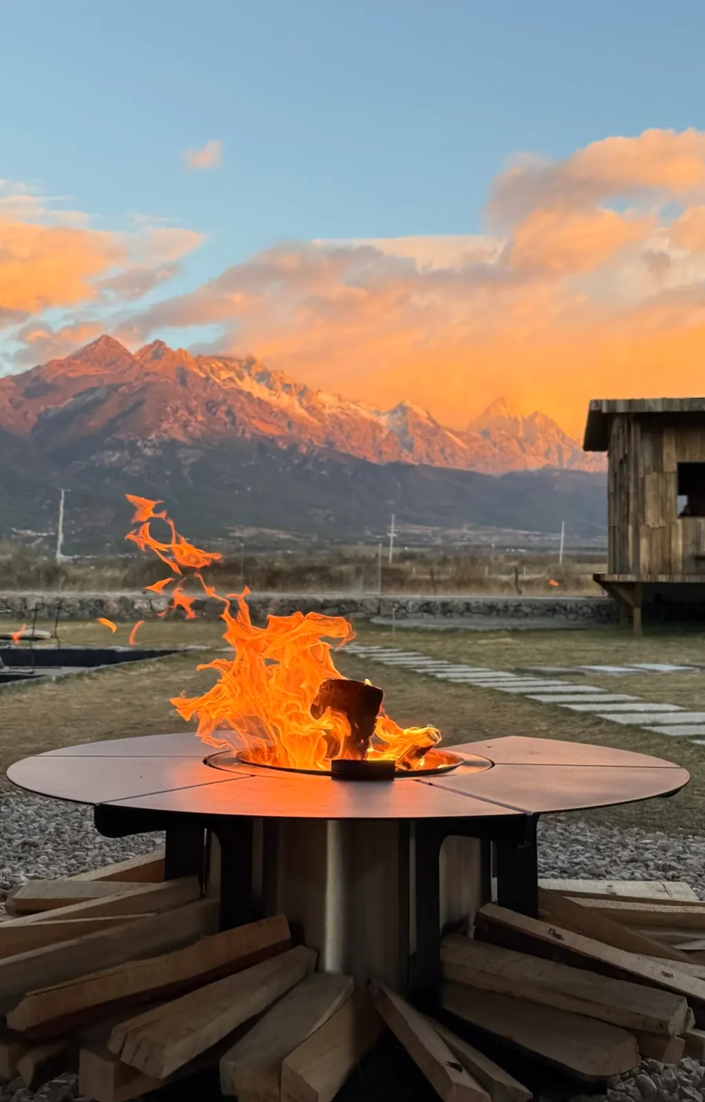 丽江玉龙雪山：夕阳染红远山，近处的篝火在松木旁燃烧